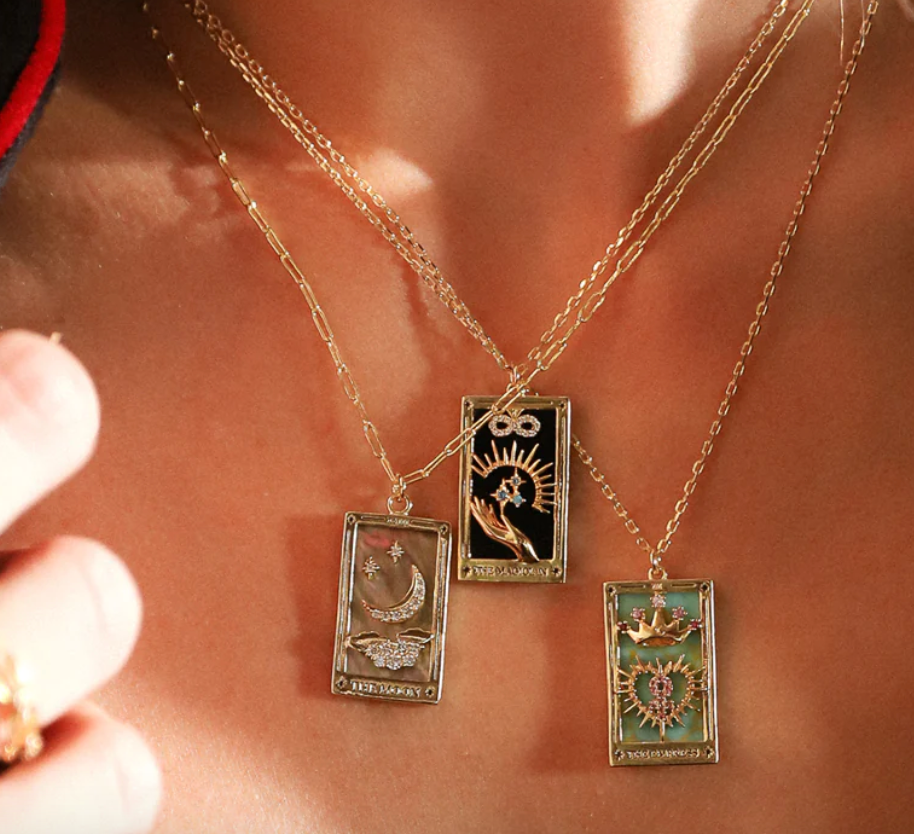 Three gold necklaces with tarot card pendants on a person's neck.