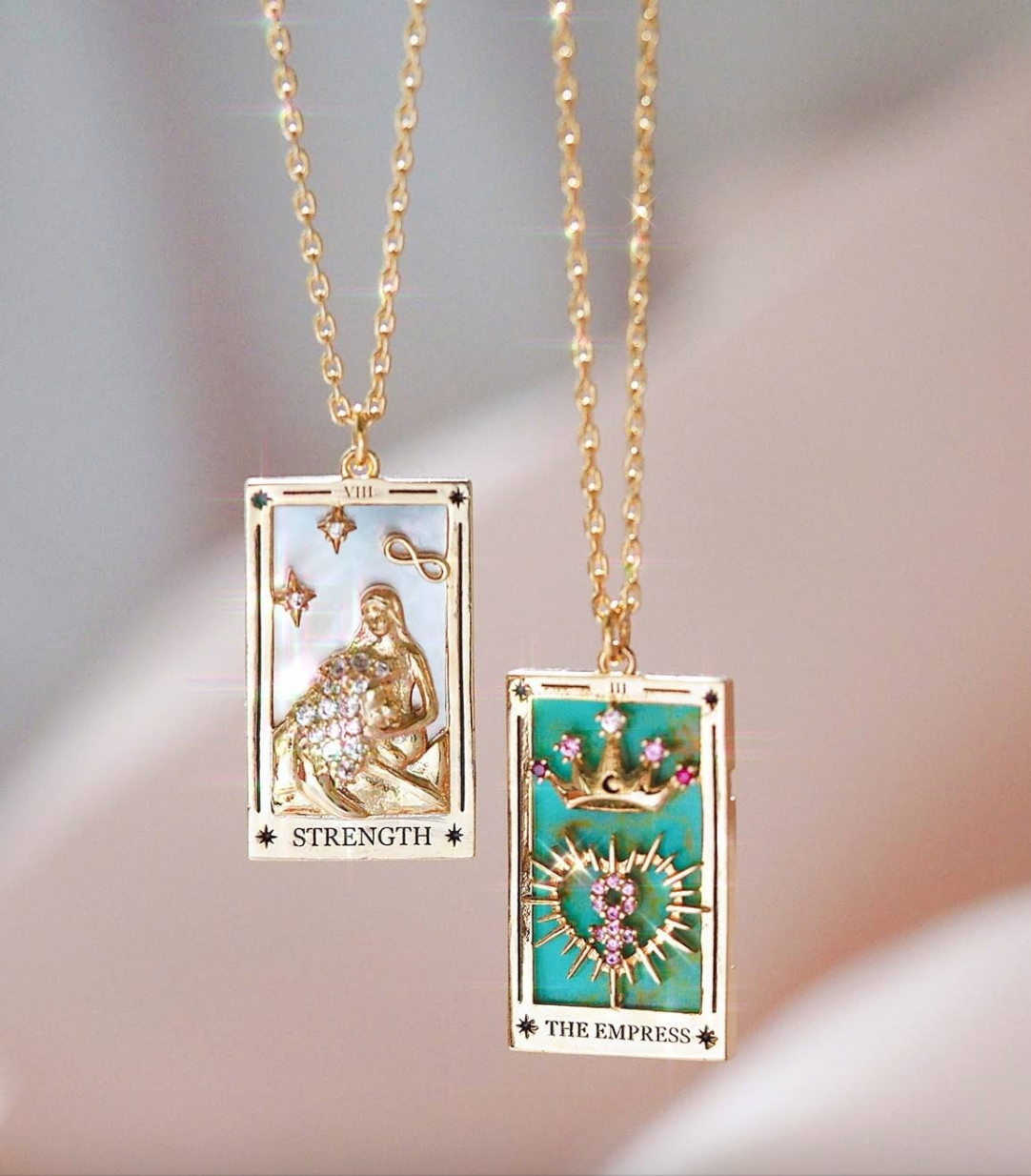 Two tarot card-themed necklaces on gold chains with a soft background.