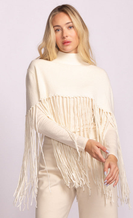 Woman wearing a cream-colored turtleneck sweater with fringe details on a light purple background