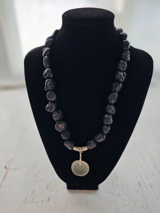 Black smooth stone necklace with a pendant on a black stand against a white background