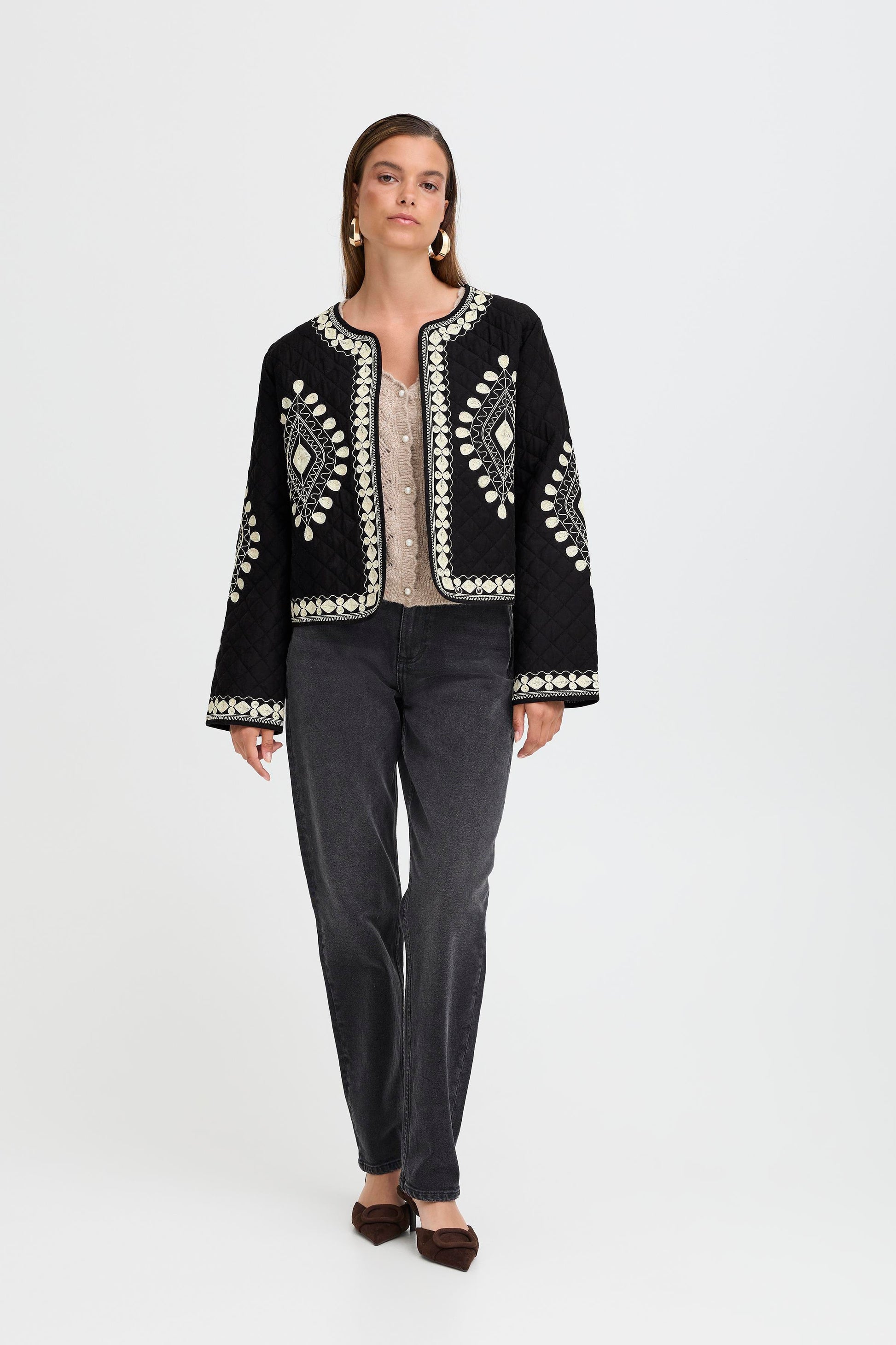 Woman wearing a black embroidered jacket and gray pants on a white background