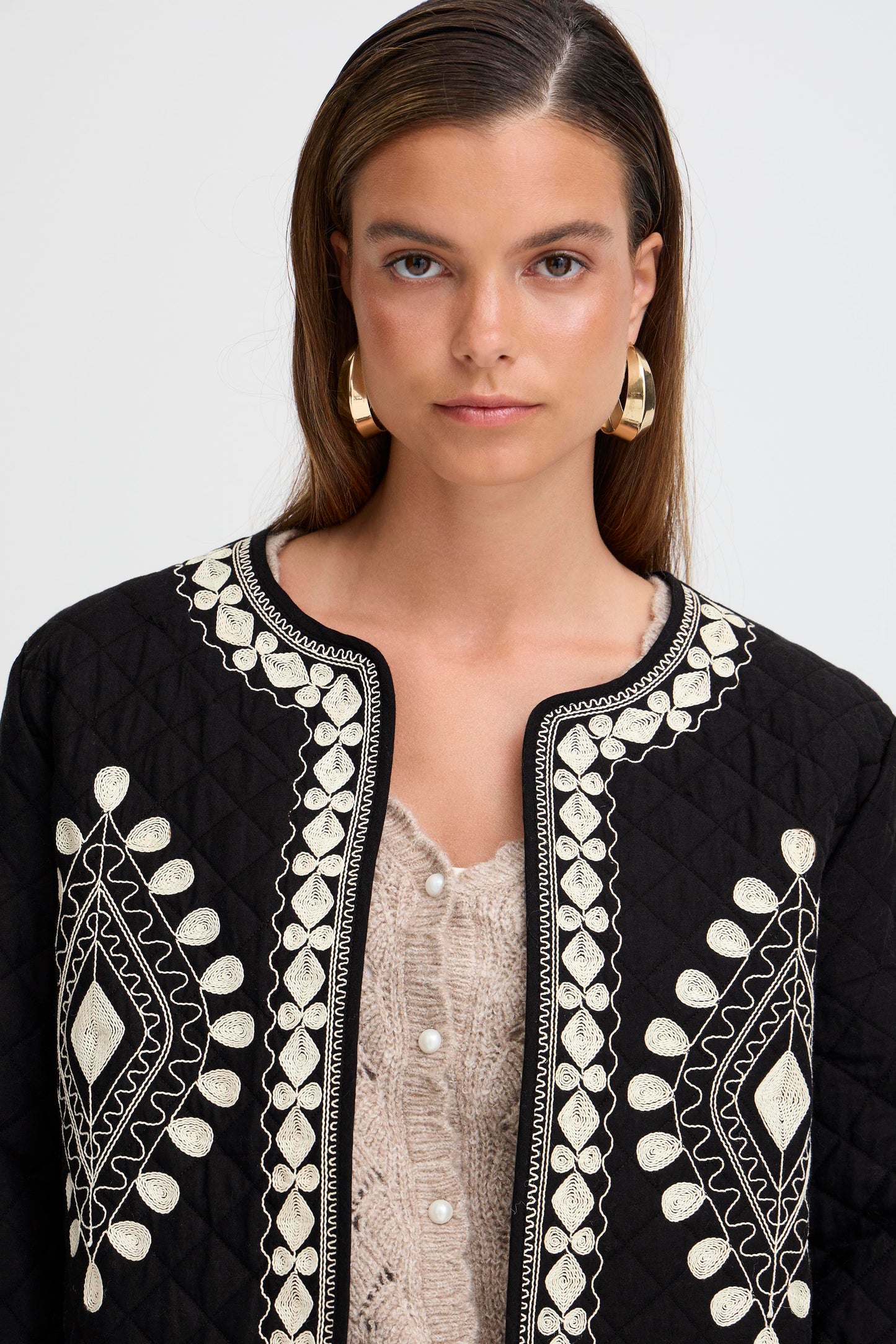 Woman wearing a black embroidered jacket with a plain background