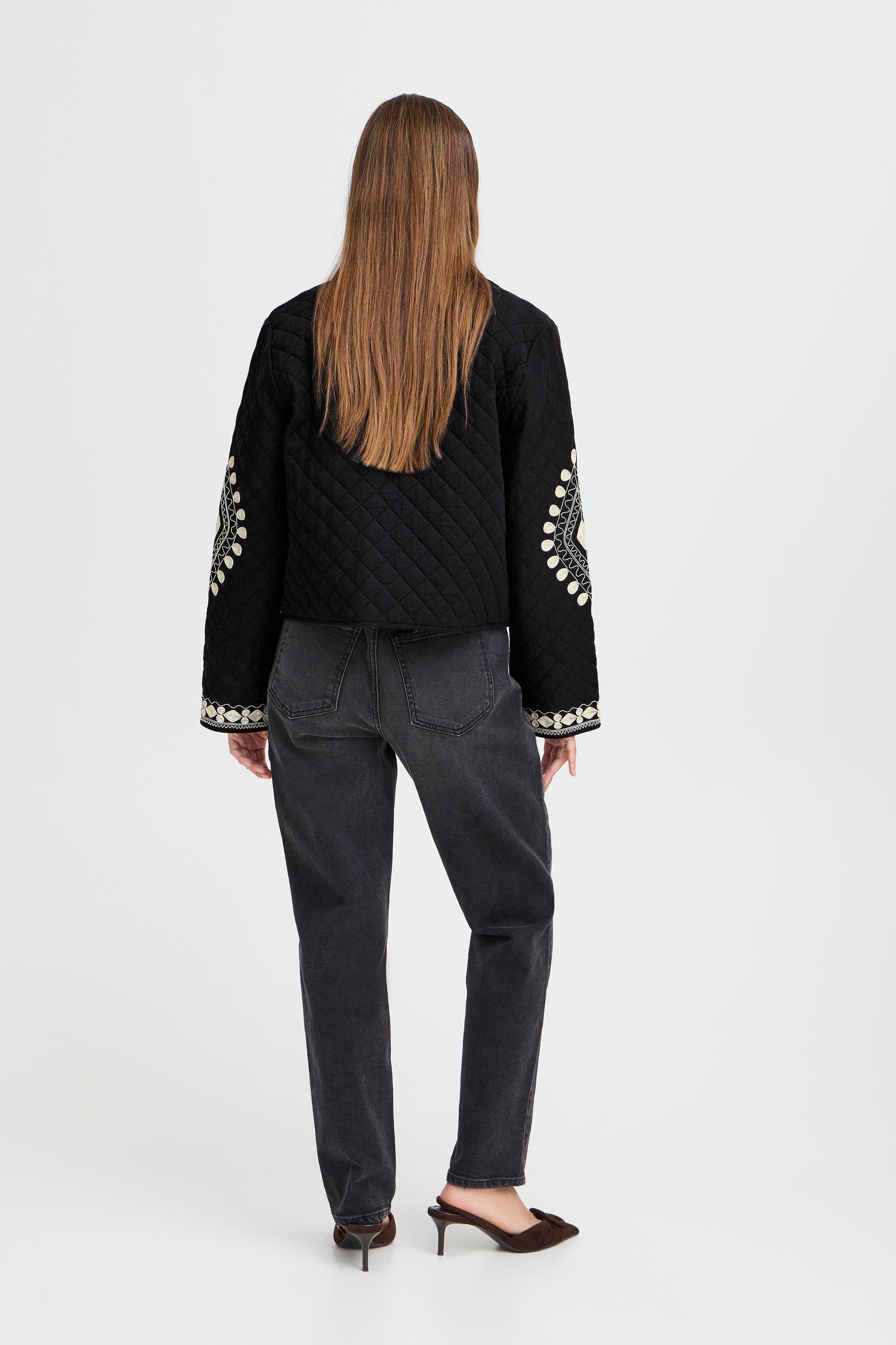 Person wearing a black jacket with white embellishments and gray pants on a white background