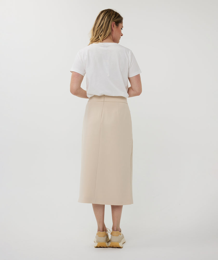 Woman wearing a white t-shirt and beige skirt on a plain background