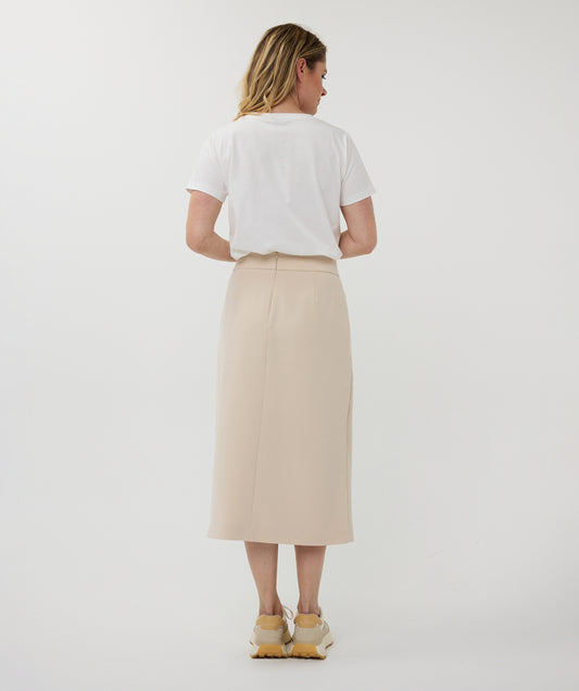 Woman wearing a white t-shirt and beige skirt on a plain background