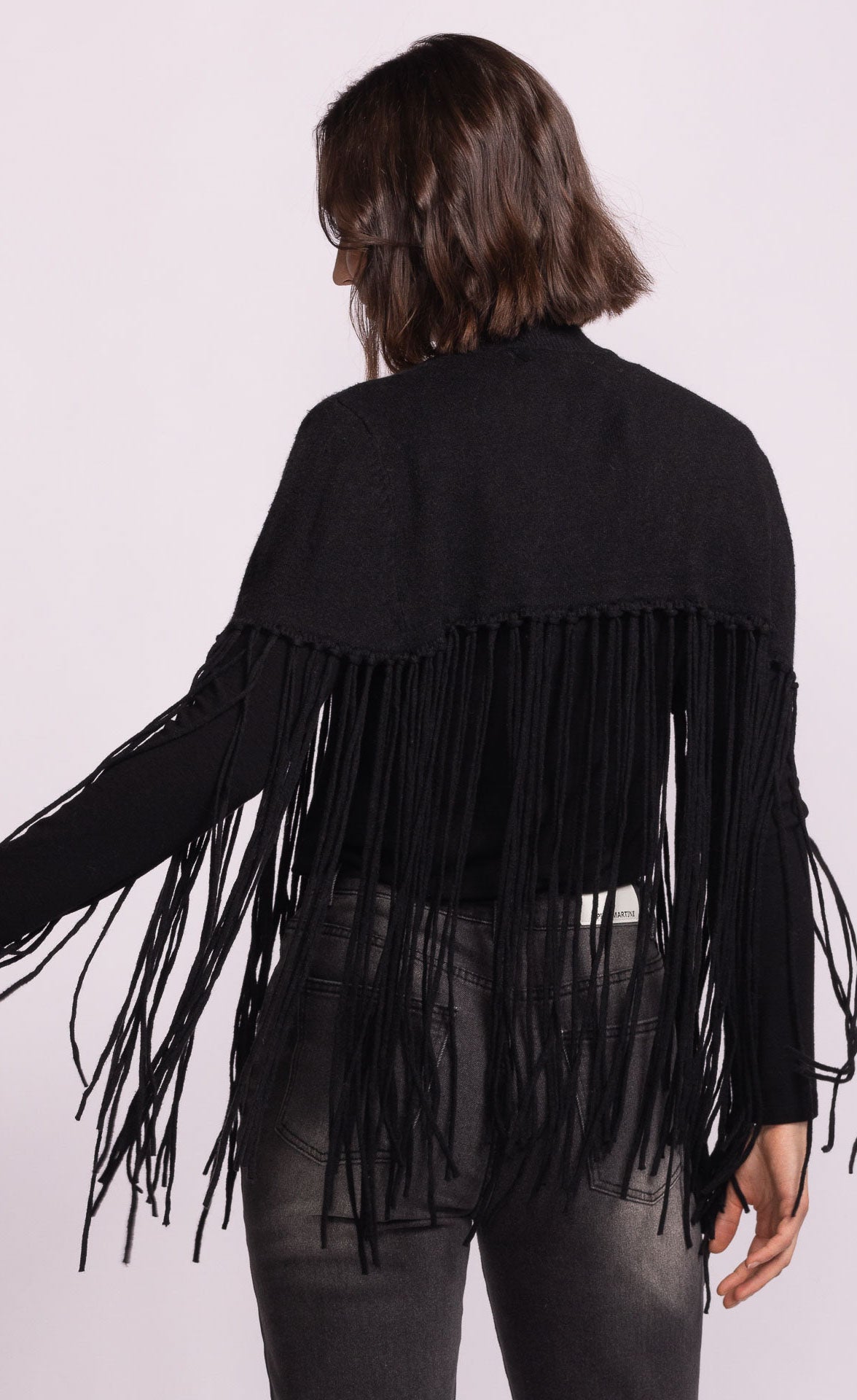 Black fringe jacket worn by a person on a light pink background