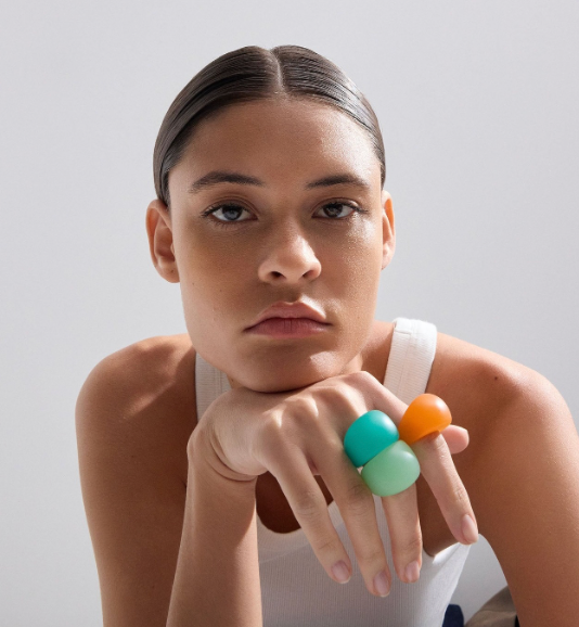 Woman wearing colorful rings on a plain background