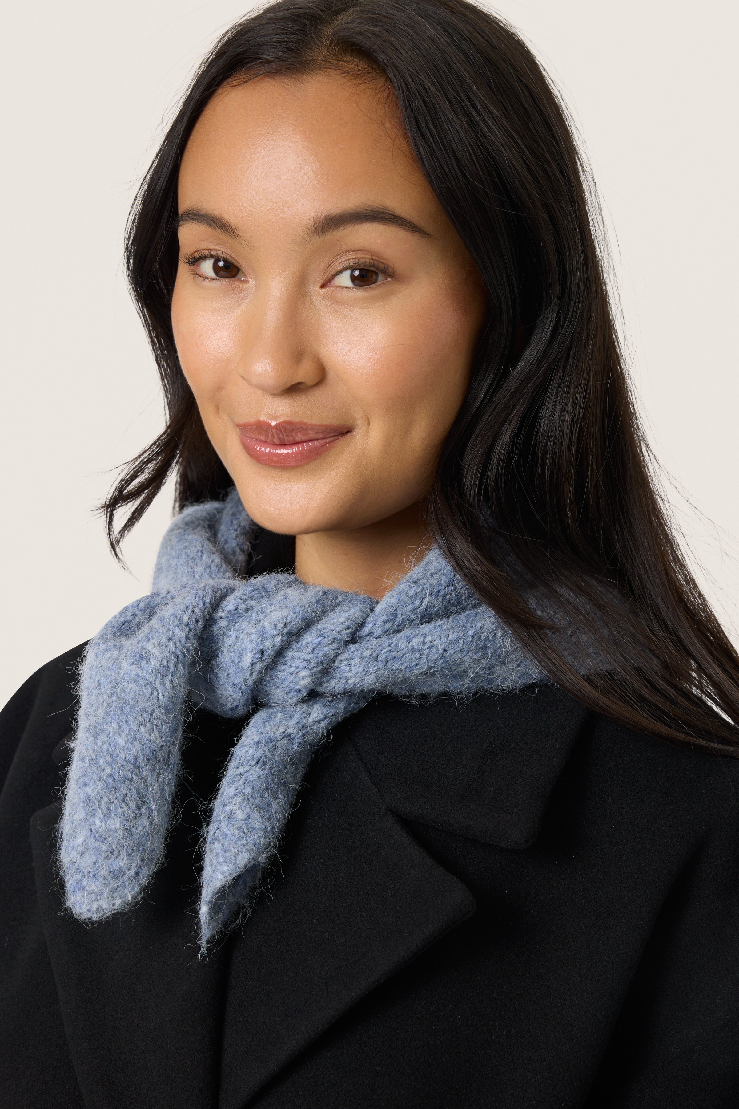 Woman wearing a blue scarf and black coat against a white background