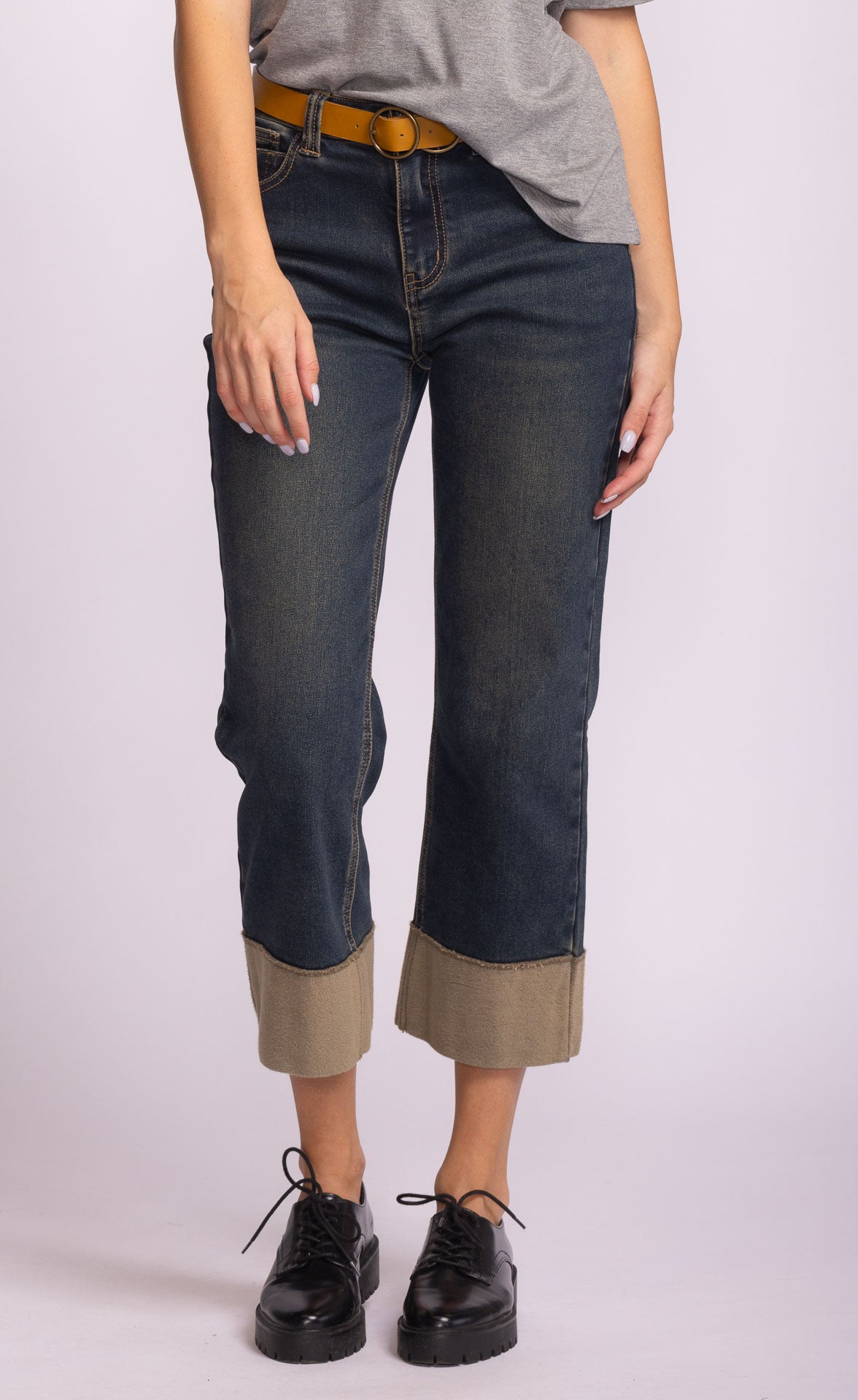 Woman wearing dark blue jeans with rolled-up cuffs and a brown belt 