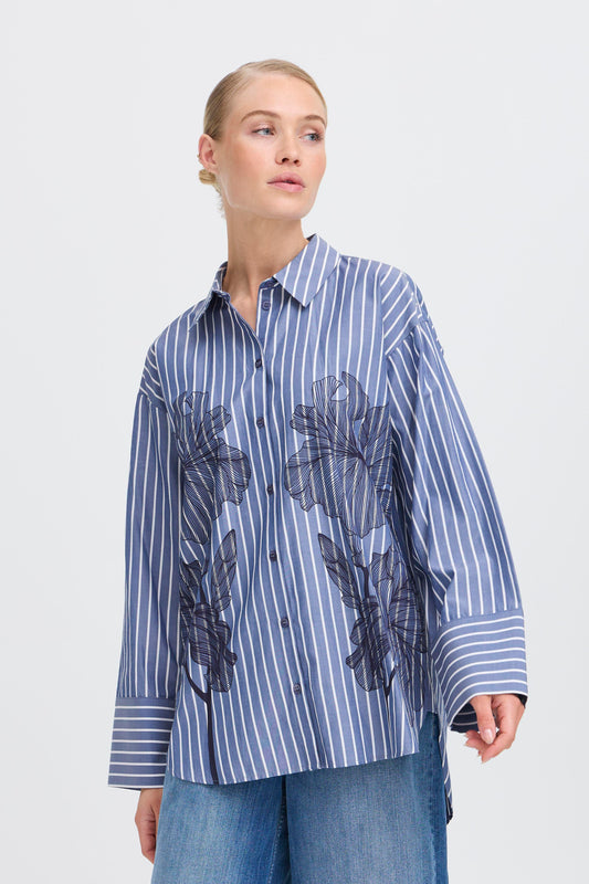 Woman wearing a blue and white striped shirt with floral print on a plain background